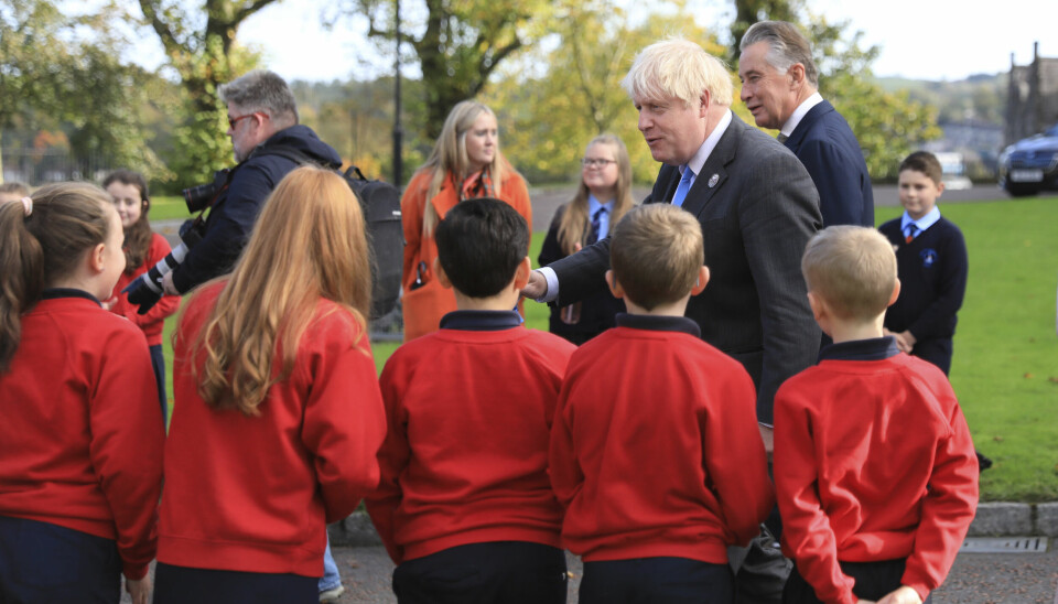 SKOLEUNIFORMER: I flere land er det vanlig at elever har egne uniformer på skolen. Bildet er tatt i Nord-Irland under et besøk av britenes daværende statsminister Boris Johnson. Bildet viser britenes statsminister i 2021, Boris Johnson, som besøker Nord-Irland. Fremme i bildet står barn med skoleuniformer. Foto: Peter Morrison / AP / NTB