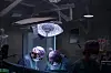 Bildet viser tre kirurger inne på en operasjonssal. En stor lampe henger over dem, og de ser ned på en pasient. Pasienten er dekket for av et laken og er ikke synlig i bildet.