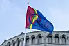 Samisk flagg vaier foran Stortingets bygning i Oslo mot lys blå himmel.