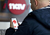 Mann sett bakfra holder en mobiltelefon med NAV-logo foran et stort NAV-skilt.