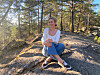 Person sitter på en solbelyst fjellknaus omgitt av furutrær i skogen.