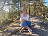 Person sitter på en solbelyst fjellknaus omgitt av furutrær i skogen.