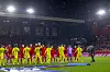 To fotballag står oppstilt på gresset foran tribunene under en kveldskamp på Brann stadion.