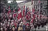 Folketog med mange norske flagg går gjennom en gate med tilskuere og bygninger i bakgrunnen i Oslo i 1945.