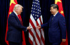 Donald Trump og Xi Jinping håndhilser foran amerikanske og kinesiske flagg på en scene.