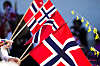 Norske flagg i rødt, hvitt og blått vaier foran en utendørsscene med mennesker i bakgrunnen.