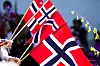 Norske flagg i rødt, hvitt og blått vaier foran en utendørsscene med mennesker i bakgrunnen.