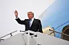 Donald Trump står i trappen til et fly og vinker ved en flyplass.