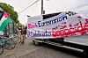 Mann holder et stort protest-banner og palestinske flagg ved en varebil utenfor Eurovision-området i Wien.