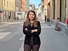 En kvinne står med armene i kors i en gate med bygninger på begge sider.