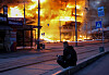 En person sitter foran en brennende bygning etter et angrep i Kyiv.