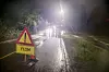 Et gult flomskilt står ved en vannfylt vei i mørket, med lys fra biler i det fjerne.