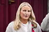 Kronprinsesse Mette-Marit står foran røde gardiner med pustemaskin på nesen.