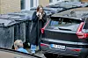 Tre personer går mellom parkerte biler ved en bygning, mens én holder en hånd foran ansiktet.