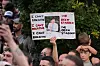 Folkemengde protesterer foran politistasjonen mens en person holder opp et skilt med et bilde.