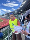 To frivillige står ved tribunen og ser på papirer under et friidrettsarrangement på stadion.