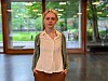 Ung kvinne står foran store vinduer i et lyst rom med grønt landskap utenfor.