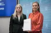 Camilla Bernt gir en rapport til barne- og familieminister Lene Vågslid foran blå bakgrunn.