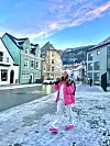 Dahlia går i en snødekt gate med fargerike hus og rosa vinterklær.