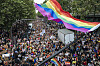 Stor folkemengde i Pride-marsj i Paris under et stort regnbueflagg.