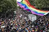 Stor folkemengde i Pride-marsj i Paris under et stort regnbueflagg.