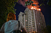 Bildet viser en dame som ser på en boligblokk som brenner i Kyiv. Foto: Danylo Antoniuk / AP / NTB
