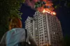 Bildet viser en dame som ser på en boligblokk som brenner i Kyiv. Foto: Danylo Antoniuk / AP / NTB