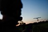 Silhuett av en soldat i forgrunnen mens en drone flyr mot kveldshimmelen over et åpent landskap.