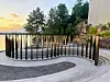 Sirkelformet uteplass med svarte stolper ved vannkanten i solnedgang.