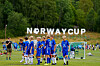 En gruppe fotballspillere i blå drakter står på en gressbane foran et mål, med Norge Cup-skilt i bakgrunnen.