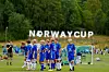 En gruppe fotballspillere i blå drakter står på en gressbane foran et mål, med Norge Cup-skilt i bakgrunnen.
