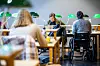 Studenter sitter ved bord i en lesesal med grønne bordlamper og dataskjermer.