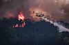 Canadair-fly slipper vann over en skogbrann med flammer og tykk røyk over skogkledde åser.