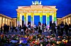 Folk og blomster foran Brandenburger Tor, som lyser med teksten «Berlin, frihetens by» og regnbuefarger.