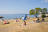 Badestrand på Huk i Oslo med solbadere, sykler, tre og rolig sjø en varm julidag.