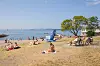 Badestrand på Huk i Oslo med solbadere, sykler, tre og rolig sjø en varm julidag.