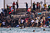 Store grupper migranter samler seg ved en steinete strand ved en grensemur ved Ceuta.