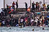 Store grupper migranter samler seg ved en steinete strand ved en grensemur ved Ceuta.