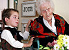 Gutt gir blomster til Jeanne Calment i et pleiehjem, med en bukett på bordet i forgrunnen.