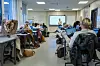 Lærer underviser elever i et klasserom med skjermer, pulter og elever som sitter vendt mot tavlen.