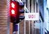 UDI-skilt på vegg ved en bygning, med røde lys og uskarpt bymiljø i bakgrunnen.