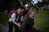 To kvinner og en mann går eller sykler gjennom et grønt festivalområde med mange mennesker i bakgrunnen.