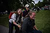 To kvinner og en mann går eller sykler gjennom et grønt festivalområde med mange mennesker i bakgrunnen.