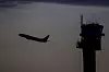 Siluett av et fly som letter og et flytårn i bakgrunnen på kvelden.