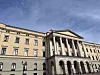 Det norske slottet i Oslo sett nedenfra med søyler, flagg på taket og blå himmel.