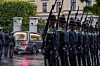 En kistebil ankommer Slottet mens soldater står oppstilt i æresvakt i regnvær.