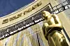 Gullfarget Oscar-statuett foran inngangen til Dolby Theatre under en klar himmel.