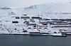 Luftfoto av Barentsburg med bygninger, kai og snødekte fjellsider ved sjøen.
