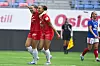 To Brann-spillere i røde drakter feirer på banen mens en Vålerenga-spiller står i bakgrunnen.