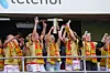Brann-spillere i røde og gule drakter jubler på en tribune og løfter en sølvpokal.
